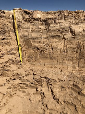 Upper part of an excavated pit: sandy walls and a folding rule for size comparison.
